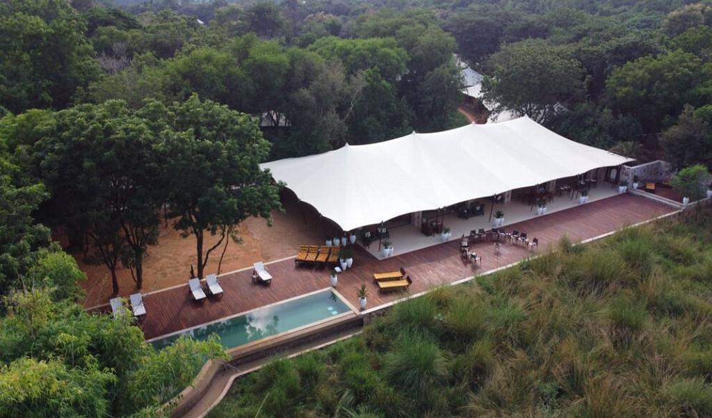 A large white hospitality tent beside a pool, surrounded by trees